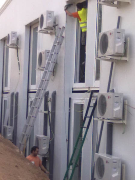 Dos trabajadores instalando aires acondicionados en un bloque de apartamentos